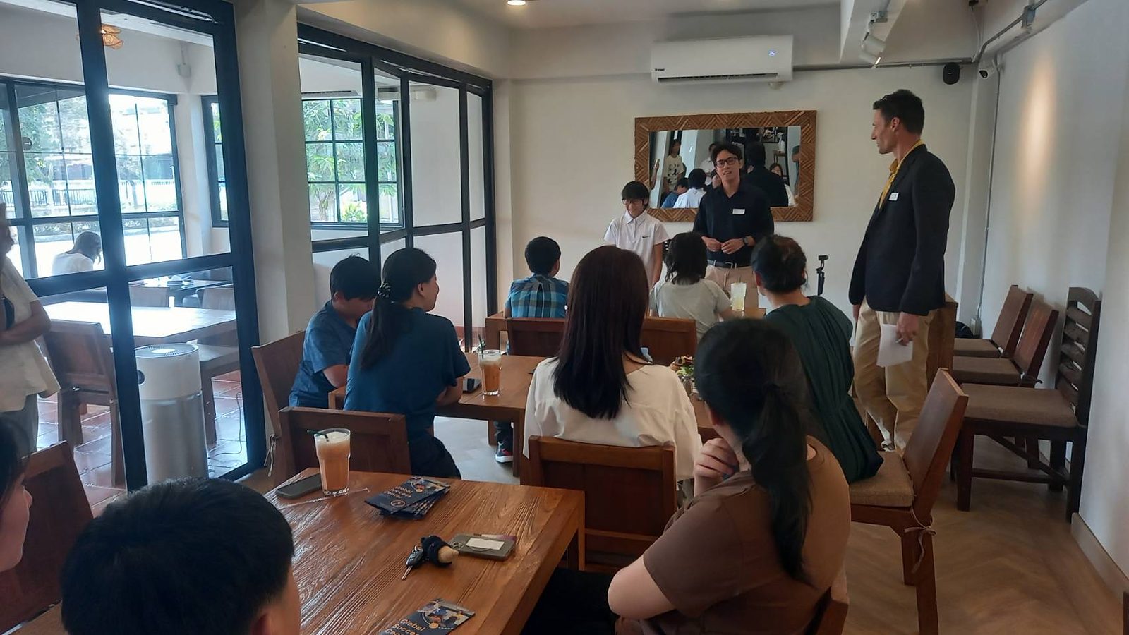 GSC students and a teacher speaking to an audience seated at a cafe